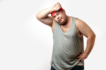 Overweight caucasian man wearing red handband takes a break, tired after training, with hand on forehead against white background with copyspace