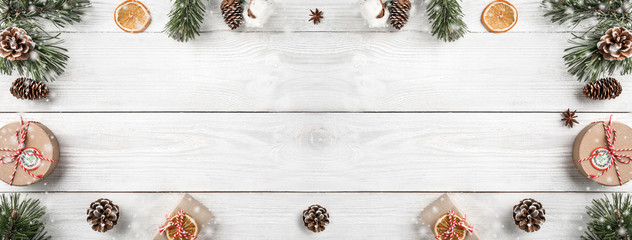 Creative frame made of Christmas tree branches on white wooden background with gift boxes, pine cones. Xmas and New Year theme. Top view, flat lay, wide composition