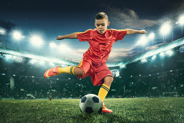 Obraz na płótnie Canvas Young boy with soccer ball doing flying kick at stadium