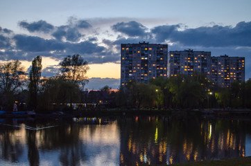Apartment buildings with glowing windows near the pond at the evening.