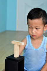 A kindergarten Asian boy concentrating on playing with wooden blocks on light wooden ceramic floor tiles during the summer, kid learning concept, child education, selective focus with copy space 
