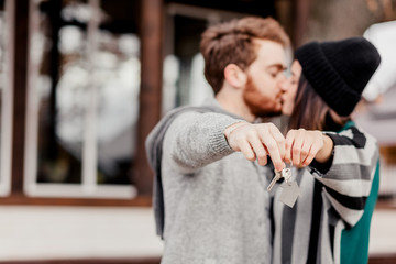Happy couple hugging, kissing outdoors, showing to camera the key of a new house . Real Estate Purchase.