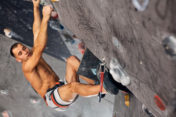 Athletic shirtless man bouldering at an indoor climbing centre. Professional climber climbing wall...