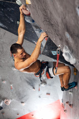 Top view of a professional man climber on a commiting route paricipating in contest, climbs upside down indoors in bouldering gym.