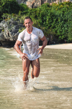 Muscular young sexy wet man runs along the beach in wet t-shirt