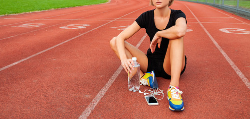 Woman runner in sportswear sitting on running stadium after run