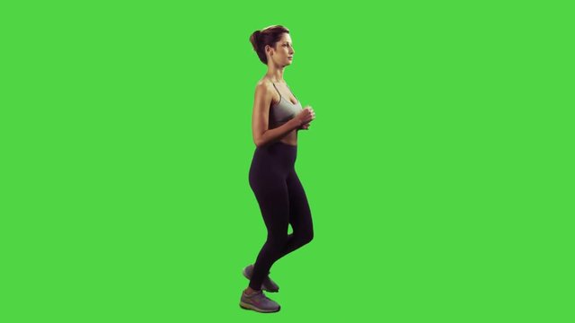 A young woman running and smiling in a full body sideways shot over a green screen.