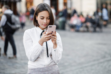 Portrait of a beautiful woman using mobile phone while standing on blurred street background.