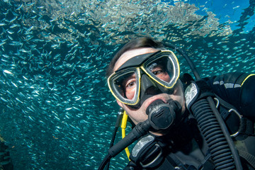 Scuba diver portrait while diving Inside a school of fish underwater
