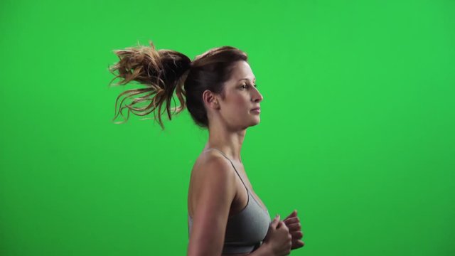 A young woman running in a medium frontal shot over a green screen, wearing a sport bra, smiles.