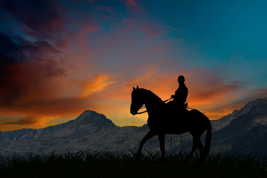 Silhouette of a horseman riding on horseback at sunset by mountains