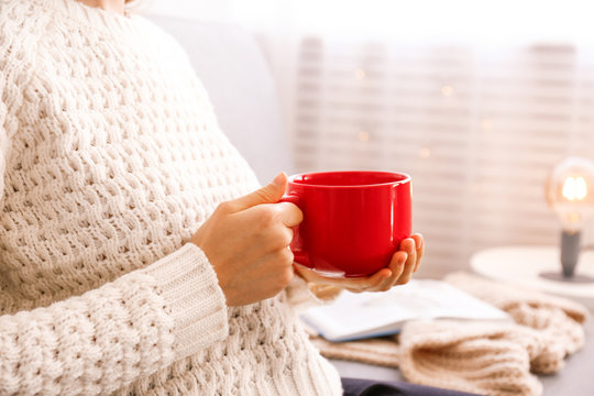 Close Up Young Woman's Hands Holding Big Cup Of Hot Beverage. Female Wearing Fashionable Oversized White Knitted Sweater, Sitting Home With Mug Of Coffee. Background, Copy Space.