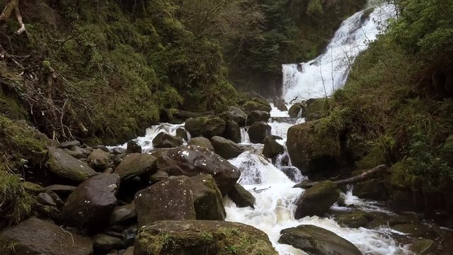 Slow ascending dolly shot as camera rises over the rocks and flowing water in this autumn / fall nature scene.Location Torc Waterfall,part of the "ring of Kerry" in Southern Ireland