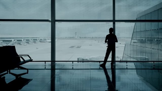 Silhouette of photographer or social media blogger or travel influencer with professional camera make photo in airport terminal, arriving and departing flights of busy hub, tourist lifestyle