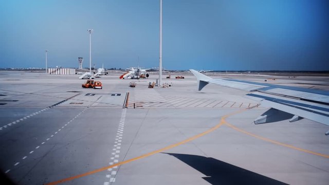 Vintage retro nostalgic look from 80s on airplane wing from illuminator window, taking off or landing, plane or jet passes parked airport vehicles, international transfer hub, travel lifestyle