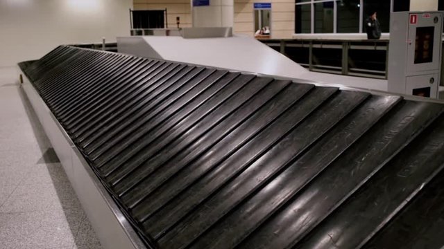 Side view on empty luggage belt moving slowly in busy terminal of international hub airport. Concept lost luggage or suitcases forever missing in airport logistics infrastructure