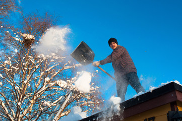 A man with a shovel removing snow from a roof