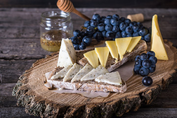 Assorted cheeses with grapes, bread, honey on dark wood background. Goat cheese with herbs. Natural wooden board. Italian appetizer. bruschetta with cheese. Still life of food. Breakfast concept.