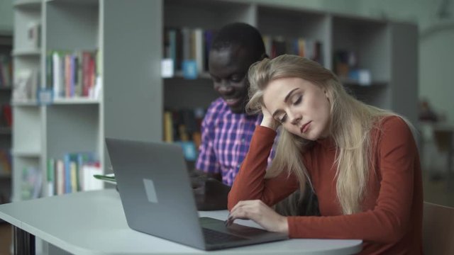 Beautiful tired girl with a laptop and her African-American friend