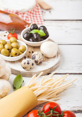 Homemade spaghetti pasta with quail eggs with bottle of tomato sauce and cheese on wooden background. Classic italian village food. Garlic, champignons, black and green olives. Vintage wooden spatula