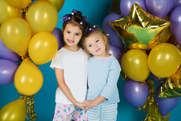 Happy little girl sisters in pajamas with balloons on a blue background