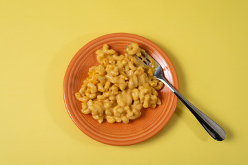 Top view of macaroni and cheese on an orange plate with fork with a yellow background.