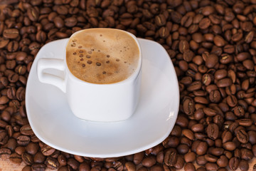  Closeup of white cup with hot coffee with foam on the coffee  beans background. selective focus. gold coffee.
