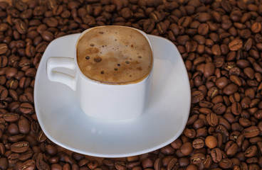  Closeup of white cup with hot coffee with foam on the coffee  beans background. selective focus. gold coffee.