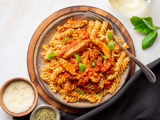 fusilli pasta with tomato sauce, chicken fillet with basil leaves on light white wooden background, top view