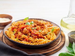 fusilli pasta with tomato sauce, chicken fillet with basil leaves on light white wooden background, side view