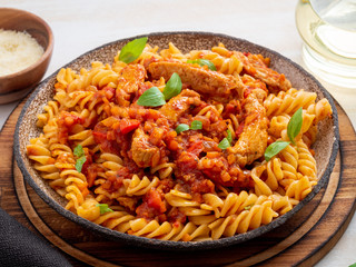 fusilli pasta with tomato sauce, chicken fillet with basil leaves on light white wooden background, side view