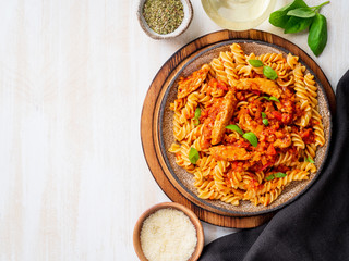 fusilli pasta with tomato sauce, chicken fillet with basil leaves on light white wooden background, top view, copy space