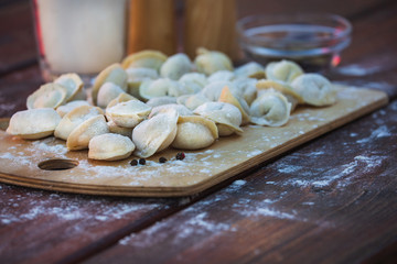 Fototapeta na wymiar Pelmeni. Homemade Raw Dumplings with Meat on Cutting Board Waiting to be Cooked. Dark Wooden Table on a Background..