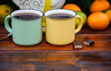 Two Mugs of Hot Tea on a Dark Wooden  Table with Chocolate Candies and Tangerines.