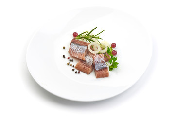 Pieces of salted herring fillet with onion ring and pepper on a white plate, isolated on a white background.