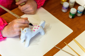 the child painting  the handmade horse with paint brushes