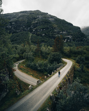 Man walking down winding mountain road bridge, Norway