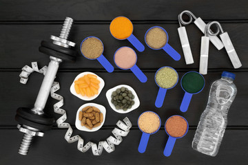 Fototapeta na wymiar Food for body builders with dietary supplement powders, water bottle, multi vitamins, fish oil and chlorella tablets with hand grippers, dumbbell weights and tape measure on wood background.