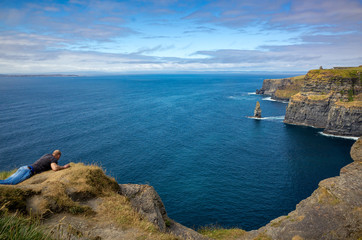 Fototapeta na wymiar Guy dangerously lean on the Cliffs of Moher, Republic of Ireland
