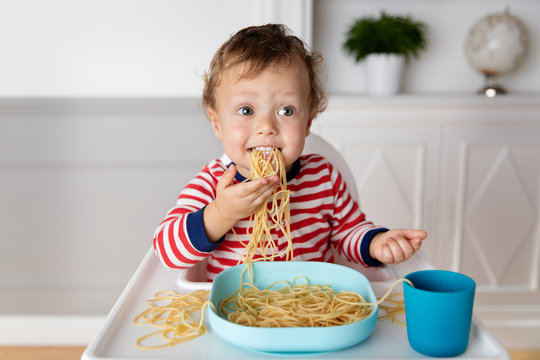 Funny baby eating a mouthful of spaghetti noodles