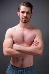 Young handsome bearded man shirtless against gray background