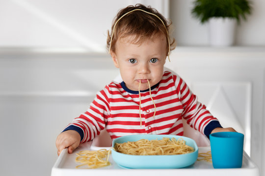 Baby making funny face while eating spaghetti noodles