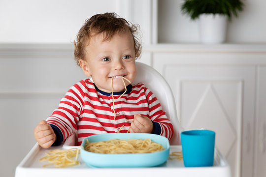 Funny toddler eating a mouthful of spaghetti noodles