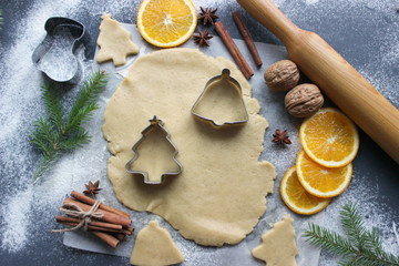 Preparation of Christmas cookies in the form of Christmas trees, fresh dough, spices scattered on the table, cinnamon, orange slices, nuts. Diet. Close-up background.