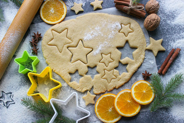 Baking Christmas cakes, dough floured on a wooden table, molds in the form of stars, spices and nuts, cinnamon sticks, oranges. Holiday atmosphere, home-made traditional pastries for new year and Chri