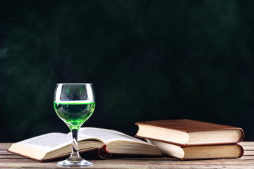 Absinthe or Green Fairy drink inspiration and muse of writers and artists. Glass on retro wooden table and books. Green smoky dark background