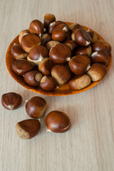 Ripe chestnuts on a plate on wooden background