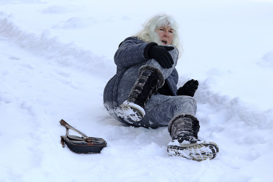 Eine Frau ist auf der winterlichen Stra&szlig;e ausgerutscht, hingefallen und hat sich verletzt. Sturz auf einer schneebedeckten Stra&szlig;e
