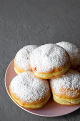 Homemade sweet donuts with powdered sugar on pink plate over grey background, side view. Copy space.