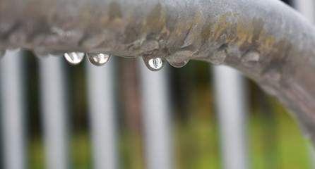 DROPS OF CRISTAL RAINING WATER DRIPPING FROM A METALLIC GREY BAR IN A RAINY DAY OF FALL